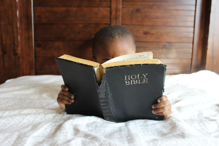 "Boy reading Bible while laying on bed" Photo by Samantha Sophia on Unsplash